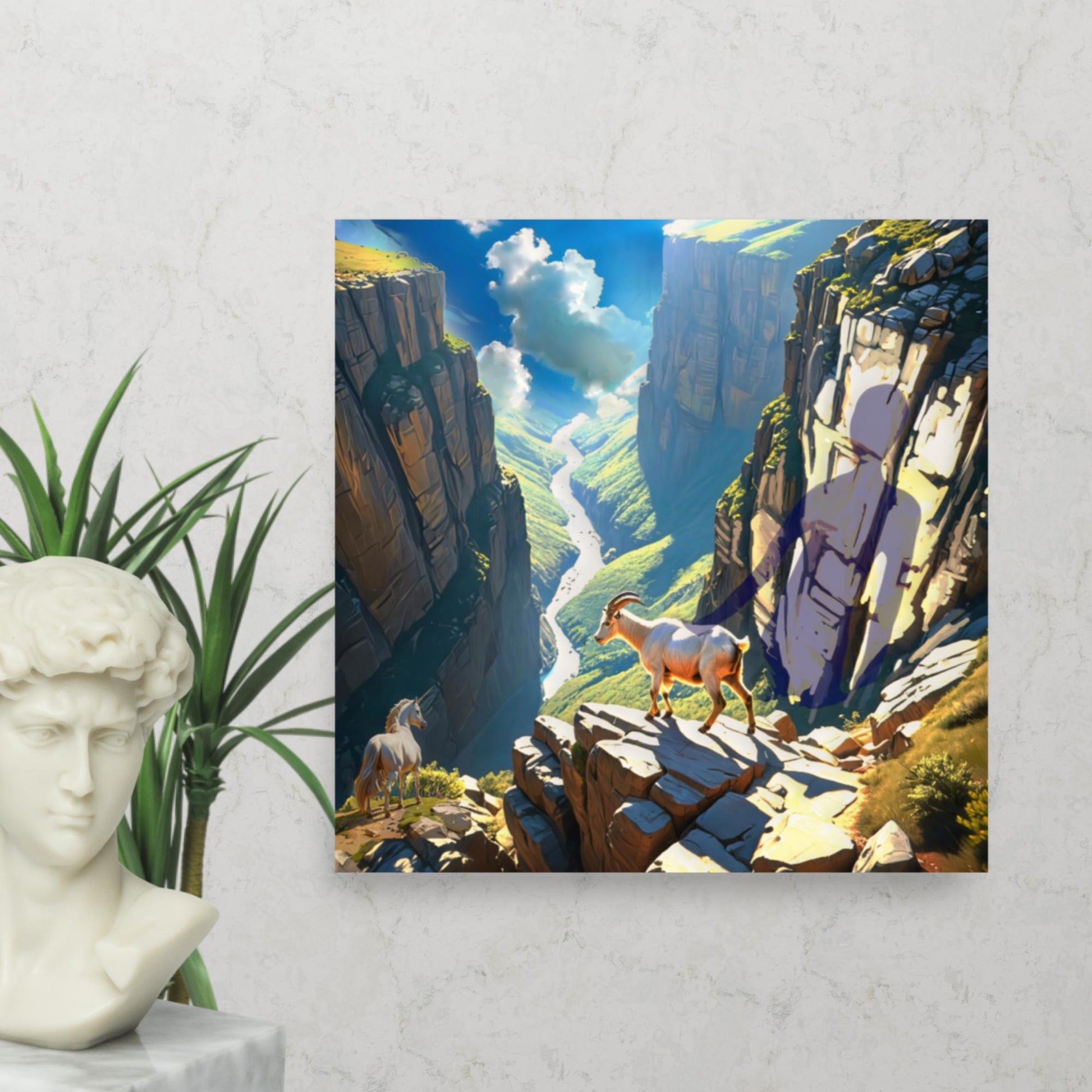 Fantasy landscape art print showing a mountain goat and unicorn perched high above a deep canyon and winding river with a mysterious shadow on the cliff wall. Displayed on a grey wall with a greek statue and plant.