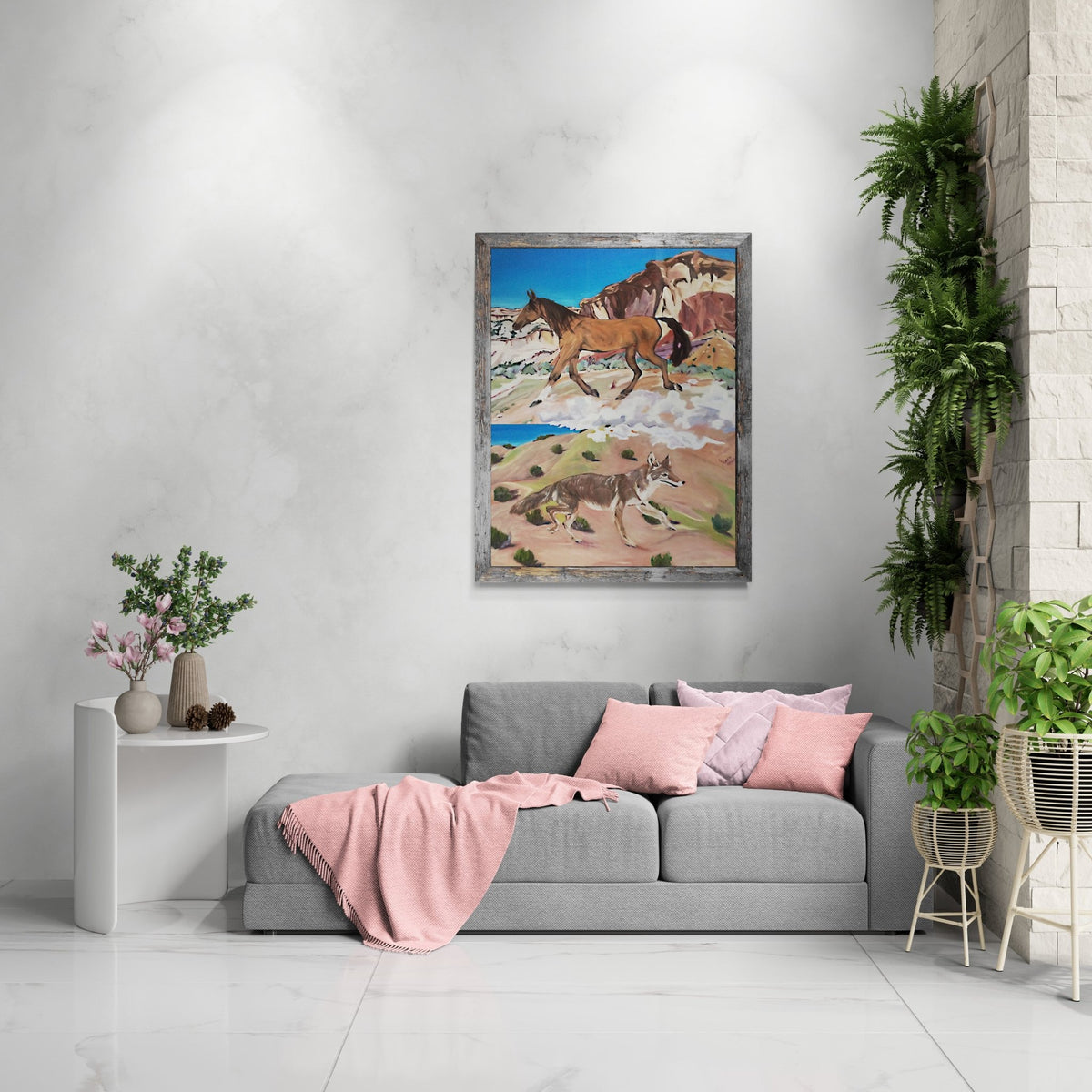 Framed Western horse and coyote painting staged above a gray sectional sofa with pink pillows