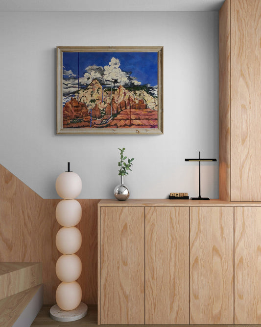 Sedona Monsoon - Framed desert canyon oil painting displayed in a minimalist Japandi interior mockup. Southwest red rock landscape wall art hanging above light wood cabinets next to a modern stacked globe floor lamp.
